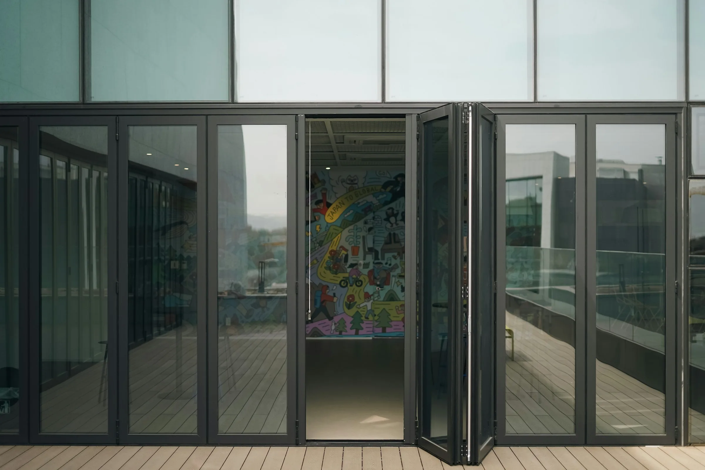 Black uPVC bi-fold doors with multiple glazed panels opening onto an outdoor deck in a modern commercial building.